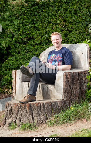 Ein Mann sitzt auf einem Sitz, geschnitzt aus einem Baumstumpf Stockfoto