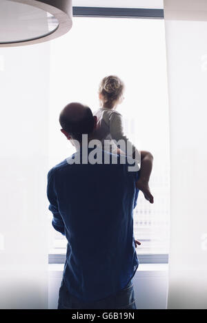 Vater Baby auf Schulter tragen, Blick aus Fenster zusammen Stockfoto