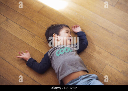 Kleiner Junge liegend am Boden vor Lachen Stockfoto