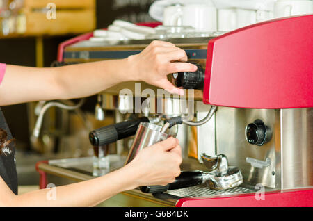 Weibliche Hände arbeiten operative industrielle Kaffeemaschine, dampfenden Milch in Metall-container Stockfoto