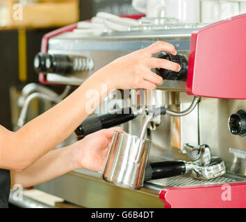 Weibliche Hände arbeiten operative industrielle Kaffeemaschine, dampfenden Milch in Metall-container Stockfoto