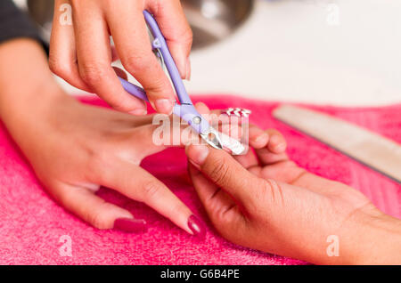 Closeup Frauen Hände Maniküre Behandlung von Frau mit Nagelschere in Umwelt, rosa Handtuch Oberfläche, verschwommenen Hintergrund Salonprodukte zu bekommen Stockfoto