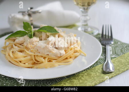 Bandnudeln mit Huhn in einer cremigen Sauce, serviert mit einem Glas Wein Stockfoto