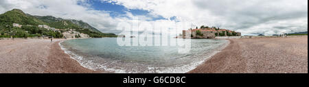 Sveti Stefan angesehen vom öffentlichen Strand zeigt dem Resort die Bucht & der Hotels an der Küste. Mit bewölktem Himmel & klares Wasser. Stockfoto