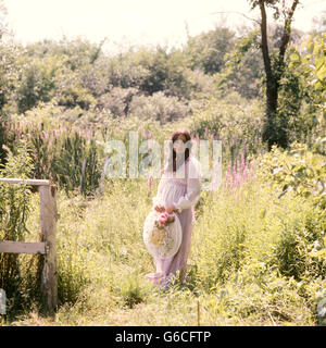 1960S 1970S SCHWANGERE FRAU IM BEREICH DER BLUMEN OMA KLEID GROßEN HUT Stockfoto