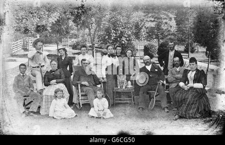 1890ER JAHRE FAMILIE GRUPPENBILD AUF RASEN DREI GENERATIONEN ERWACHSENEN TENNISSCHLÄGER ENGLISCH SETTER HUND HALTEN IN MITTE Stockfoto
