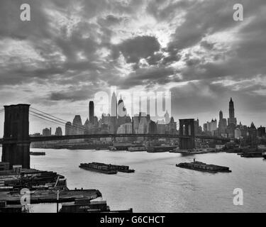 1940S 1950S DRAMATISCHEN SONNENUNTERGANG INNENSTADT LASTKÄHNE SKYLINE VON NEW YORK CITY MIT BROOKLYN BRIDGE IM EAST RIVER NEW YORK NY USA Stockfoto