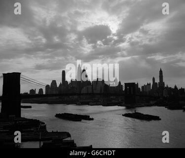 1940S 1950S DRAMATISCHEN SONNENUNTERGANG INNENSTADT LASTKÄHNE SKYLINE VON NEW YORK CITY MIT BROOKLYN BRIDGE IM EAST RIVER NEW YORK NY USA Stockfoto