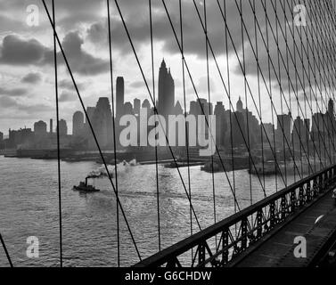 DIE SKYLINE DER INNENSTADT 1940S 1950S MANHATTAN GESEHEN DURCH KABEL DER BROOKLYN BRIDGE SCHLEPPER IM EAST RIVER NEW YORK NY USA Stockfoto