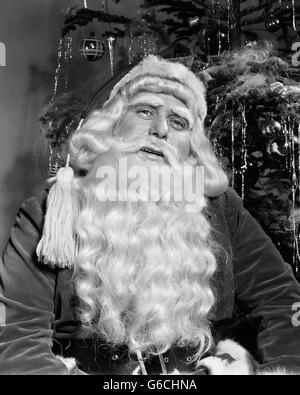 1940ER JAHRE PORTRAIT VON SANTA CLAUS VOR GESCHMÜCKTER WEIHNACHTSBAUM Stockfoto