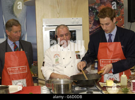 Prinz William zeigt seine Kochkünste mit einem Wok während sein Vater, der Prinz von Wales, während ihres Besuchs auf der Anglesey Food Fair auf dem Anglesey Agricultural Showground über die Präsentation der Kochkunst wacht. Stockfoto