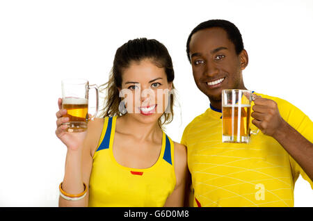 Charmantes interracial paar tragen gelbe Trikots, posiert für die Kamera hält Biergläser und lächelnd, weiße Studio-Hintergrund Stockfoto