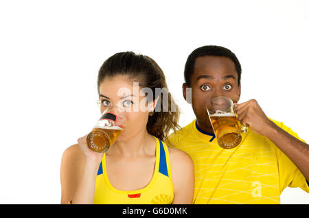 Charmantes interracial paar tragen gelbe Trikots, posiert für die Kamera hält Biergläser und lächelnd, weiße Studio-Hintergrund Stockfoto