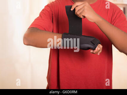Closeup Mann im roten Hemd tragen schwarze Handgelenkstütze Klammer am rechten, Klettverschluss mit anderen Arm anziehen Stockfoto