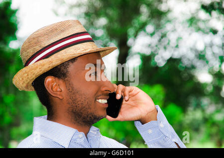 Gut aussehender Mann in blauem Hemd und Sommerhut telefonieren mit Handy und genießen Sie schöne Tag in Park Umgebung Stockfoto