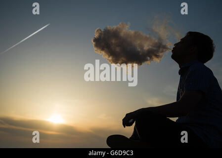 Silhouette der Mann raucht eine Pfeife in GAP bei Sonnenuntergang. Fotograf in einem Baseball-Cap, raucht eine Pfeife bei Sonnenuntergang am Meer. Reisen, Abenteuer, Meditation, Entspannung, Urlaub. Stockfoto