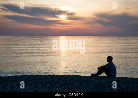 Mann-Silhouette am Strand mit Meer und Sonnenuntergang Hintergrund Stockfoto
