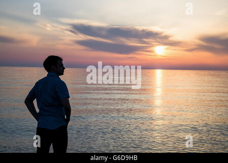 Junger Mann bei Sonnenauf- oder Sonnenuntergang am Strand vor fantastischem Meerblick stehen und über seine Zukunft nachzudenken. Ansicht von hinten Stockfoto