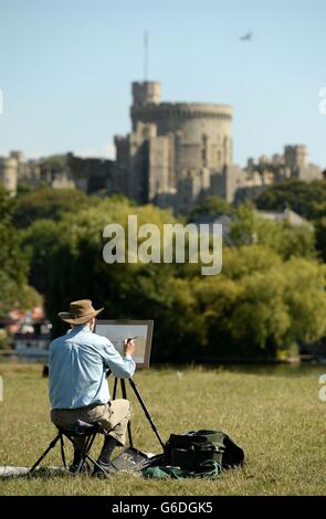 Ein Künstler malt an den Ufern der Themse im Schatten des Windsor Castle, wenn das warme Wetter anhält. Stockfoto