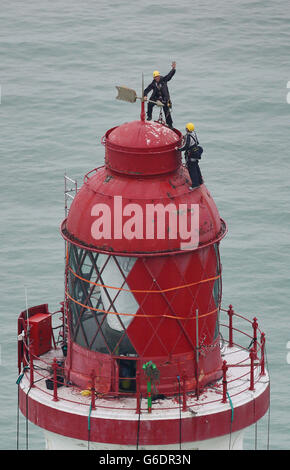 Ingenieure balancieren auf der Spitze des Beachy Head Lighthouse in der Nähe von Eastbourne, Sussex, während der Prozess der Neulackierung der Struktur nach einer erfolgreichen Spendenaktion zur Rettung der Streifen beginnt. Stockfoto