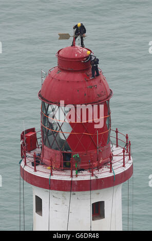 Ingenieure balancieren auf der Spitze des Beachy Head Lighthouse in der Nähe von Eastbourne, Sussex, während der Prozess der Neulackierung der Struktur nach einer erfolgreichen Spendenaktion zur Rettung der Streifen beginnt. Stockfoto