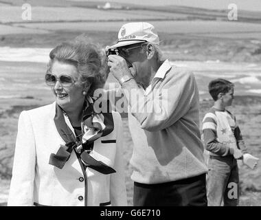 PM Mrs. Margaret Thatcher blickt auf das Meer, während Ehemann Denis einen kurzen Schnappschuss des Constantine Day in der Nähe von Padstow am Beginn ihres jährlichen kornischen Urlaubs macht. Stockfoto