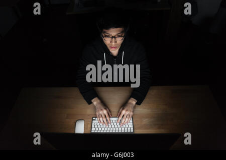 Draufsicht der asiatischen jungen Mann zu sitzen und mit Laptop im dunklen Raum Stockfoto