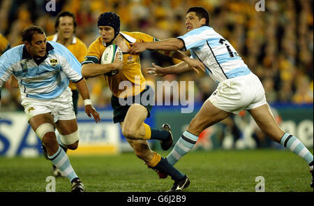 Der Australier Stephen Larkham bricht zwischen Gonzalo Longo (links) und Manuel Contepomi aus Argentinien während des australischen Sieges 24-8 im Eröffnungsspiel der Rugby-Weltmeisterschaft 2003 im Telstra Stadium, Sydney. Stockfoto