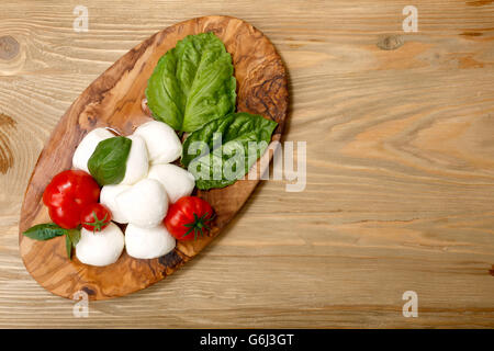 Italienische Küche. Mozzarella, Heirloom Tomaten, Basilikum-Blätter auf einem hölzernen Teller. Flach zu legen Stockfoto