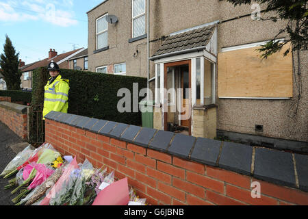 Ein Polizeibeamter steht vor dem Ort eines Hausfeuers auf der Williamthorpe Road in North Wingfield, Chesterfield, wo nach dem Tod von vier Menschen, darunter zwei Kinder, Blumen-Tribut verausgibt wurde. Stockfoto