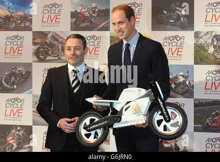 Der Herzog von Cambridge erhält ein Geschenk für seinen Sohn Prinz George vom Ausstellungsleiter Dean Linehan (links) während seines Besuchs bei Motorcycle Live im NEC, Birmingham. Stockfoto