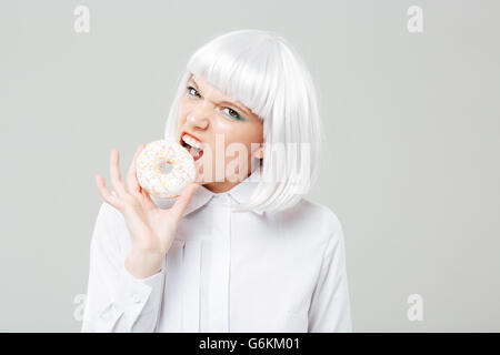Wütend hübsche junge Frau mit blonden Haaren essen frische Krapfen auf weißem Hintergrund Stockfoto