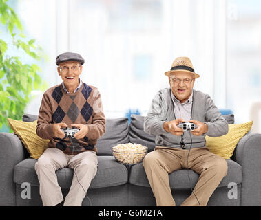 Zwei fröhliche Senioren spielen von Videospielen sitzt auf einem grauen Sofa zu Hause Stockfoto