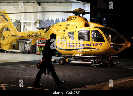 Ein Pilot geht an einem Scottish Ambulance Service Hubschrauber in seinem Hangar an seiner Basis in Glasgow City Heliport auf dem Fluss Clyde vorbei, nachdem die Einschränkungen von Bond auf Police Scotland und den Scottish Ambulance Service Hubschraubern gesetzt wurden. Stockfoto