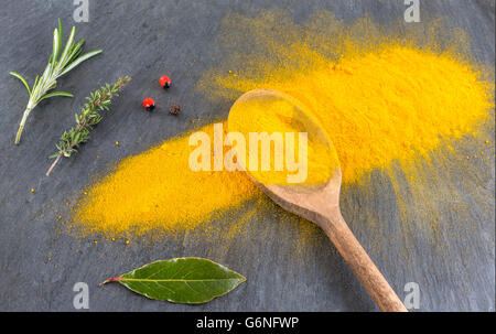 Gelbe Curry-Pulver in den Holzlöffel auf Schiefer Hintergrund isoliert. Stockfoto