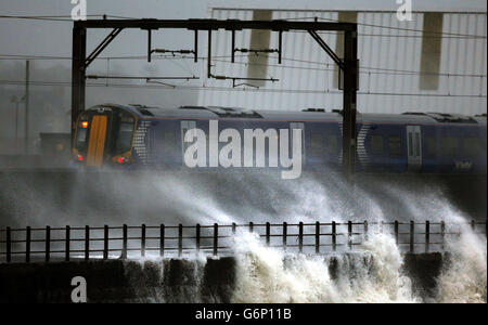 Ein Zug fährt durch die Küste bei Saltcoats in Schottland, da Großbritannien auf das Schlimmste vorbereitet ist, da eine Kombination aus hohen Gezeiten, starken Regenfällen und starken Winden erwartet wird, dass sie Teile des Landes noch schwerer überfluten. Stockfoto
