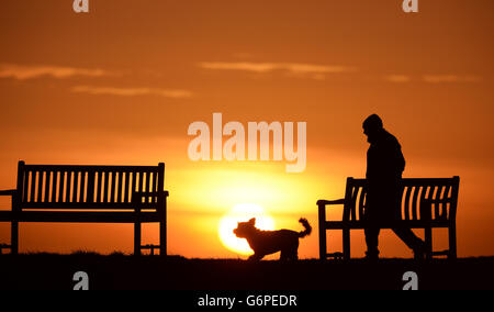 Winterwetter 24. Januar. Ein Mann geht mit seinem Hund, während die Sonne in Tynemouth aufgeht. Stockfoto