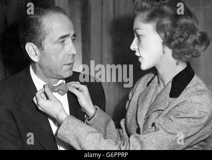 Die Schauspielerin Lauren Bacall, 27, justiert die Fliege ihres Mannes Humphrey Bogart, 50, bei einem Empfang im Claridge's Hotel, London. Stockfoto