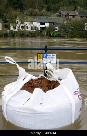 Mit dem Anstieg des Wasserspiegels auf dem Fluss Severn wurden Sandsäcke aufgestellt, um die vorübergehenden Hochwasserschutzbarrieren auf dem Wharfage in Ironbridge in der Nähe von Telford, Shropshire, abzuhalten, wobei Gärten bereits überflutet sind, die Bewohner hoffen, dass die Barrieren Überschwemmungen in ihren Häusern verhindern werden. Tausende von Eigenheimbesitzern könnten für Überschwemmungen und Senkungen Schäden an ihren Sachversicherungen geltend machen. Stockfoto