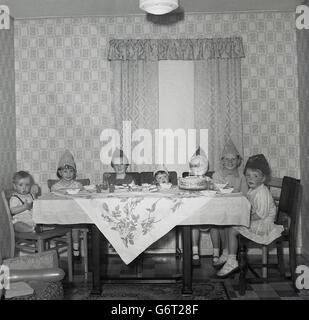 Historisches Bild von einem Kindergeburtstag der 1950er Jahre. Gruppe von Kleinkindern sitzen zusammen am Tisch in der Stube, den Kuchen zu genießen. Stockfoto