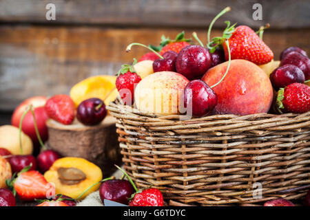 Frische reife Sommerbeeren und Früchte (Pfirsiche, Aprikosen, Kirsche und Erdbeere) im Weidenkorb Stockfoto