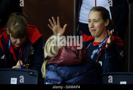 Die britische Skelett-Goldmedaillengewinnerin Lizzie Yarnold (Mitte) zeigt ihre Goldmedaille den Lockenspielern Claire Hamilton (links) und Anna Sloan, die während der Olympischen Spiele in Sotschi 2014 im Eiswürfel-Curling-Center das Gold-Medaillenspiel der Herren beobachten. Stockfoto