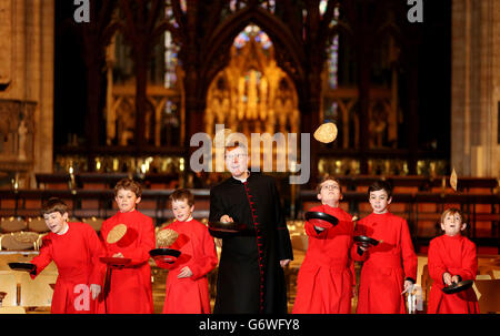 Chöre des Ely Cathedral Chores und des Reverend Mark Bonney nehmen an traditionellen Pfannkuchen-Rennen vor dem abendlichen Gesang in der Kathedrale in Cambridgeshire Teil. Stockfoto