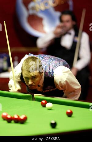 Der schottische Stephen Hendry am Tisch während seines Halbfinalmatches gegen Ronnie O'Sullivan (Hintergrund) bei den 2004 Embassy World Snooker Championships im Crucible Theatre, Sheffield. Stockfoto