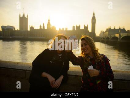 Touristen machen ein Foto, während die Sonne hinter den Houses of Parliament in Westminster, im Zentrum von London untergeht. Stockfoto