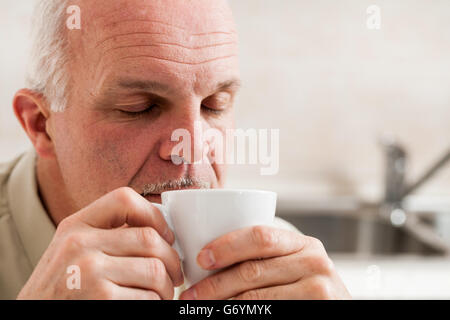Hautnah auf einzelnen bärtigen reifer Mann mit Augen geschlossen und schläfrig Ausdruck von kleinen weißen Teetasse Kaffee schlürfen Stockfoto