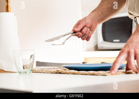 Nahaufnahme der Hand Einstellung Tabelle mit Gabel und Messer neben leeren Glas, Küchenpapier und Mikrowelle im Hintergrund Stockfoto