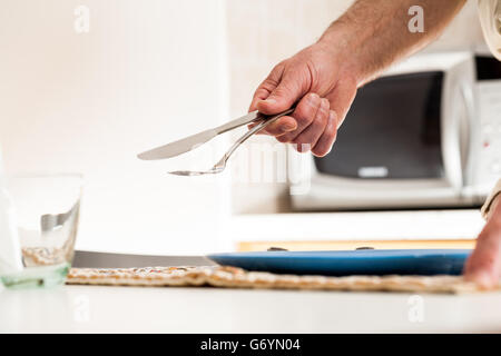 Nahaufnahme von Hand mit Messer und Gabel am Tisch mit Glas und Teller unter und Mikrowelle im Hintergrund Stockfoto