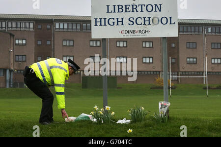 Ein Polizist legt Blumen von einem Mitglied der Öffentlichkeit vor der Liberton High School in Edinburgh, wo ein Schüler starb, nachdem eine Mauer in der Schule auf sie einstürzte. Stockfoto