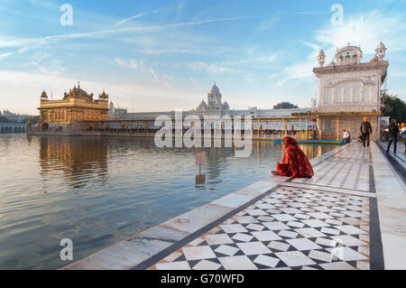 Unbekannte Frau in einem roten Sari sitzt und betet in Golden Temple Stockfoto